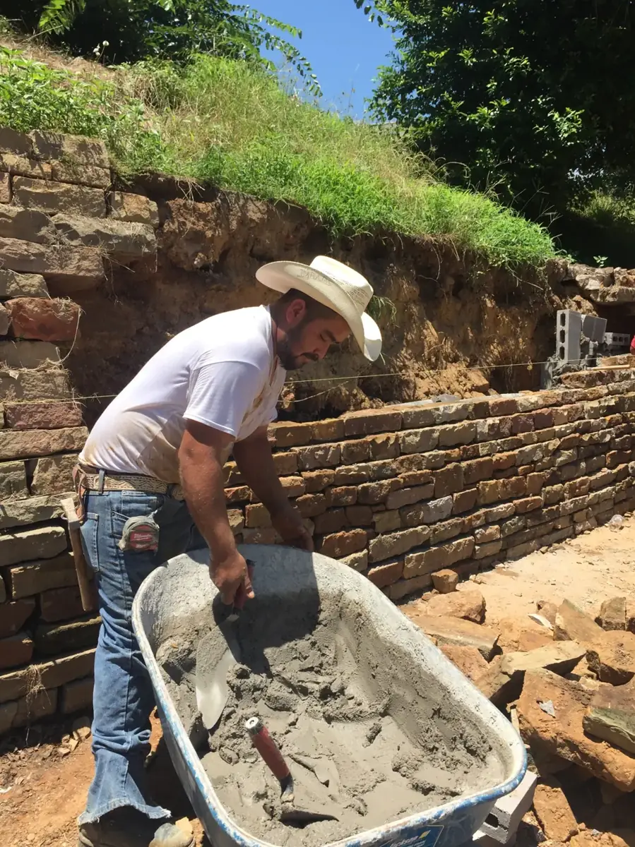 Omega Masonry mason mixing mortar beside a stacked stone retaining wall