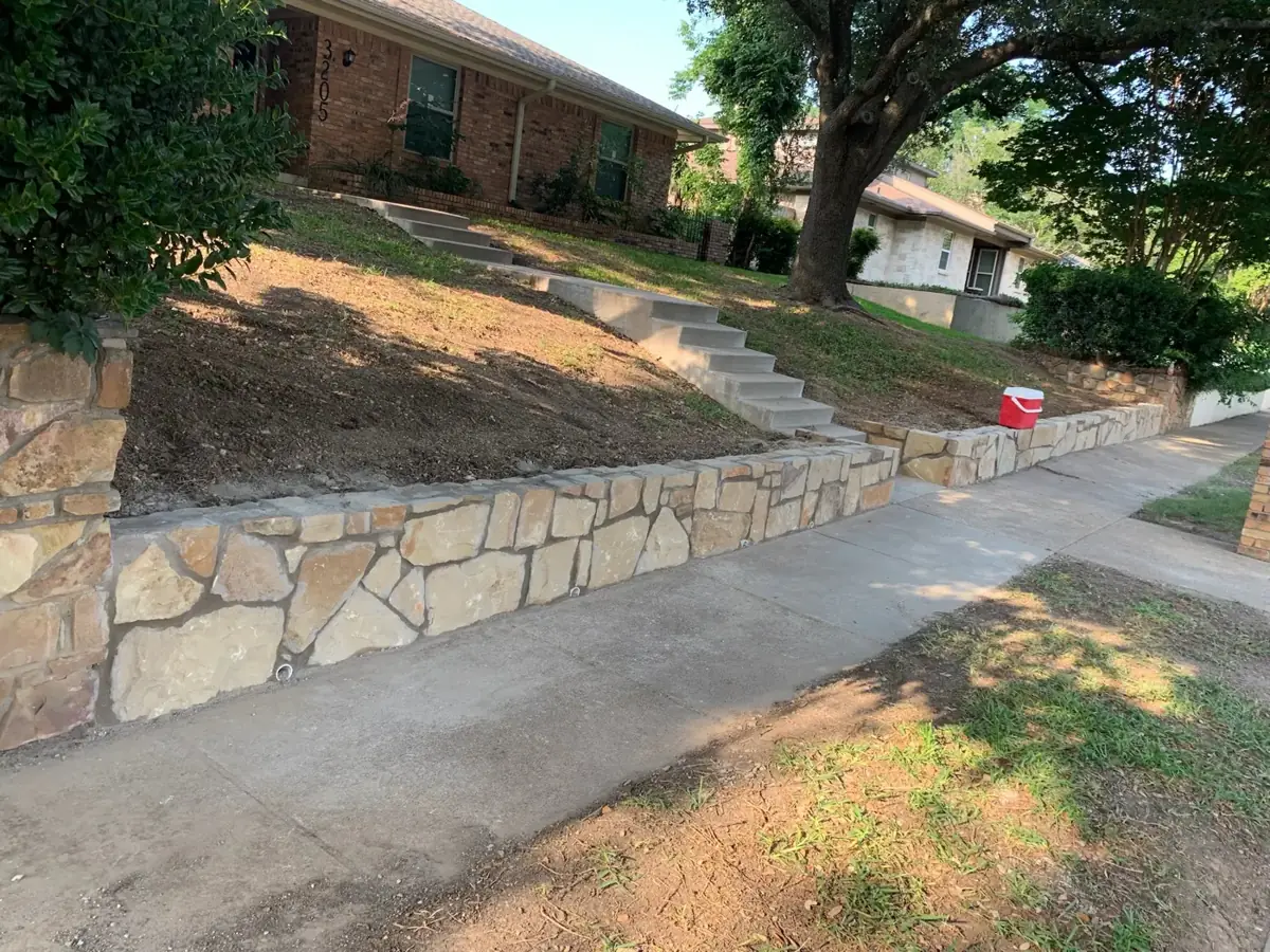 Chopped stone retaining wall and steps along a sidewalk on a sloped front yard