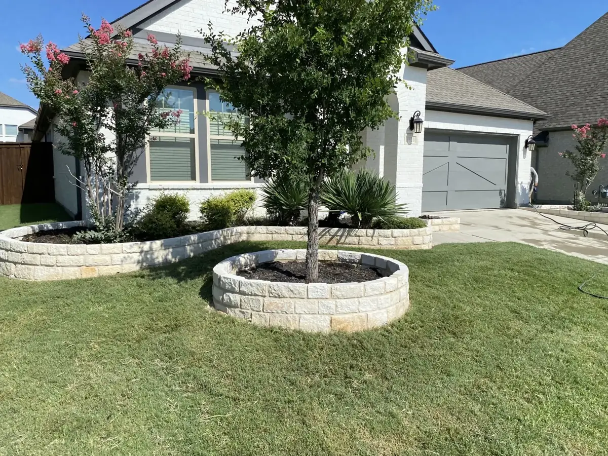 Cream stone tree ring and curved flowerbed border in front of a white brick home