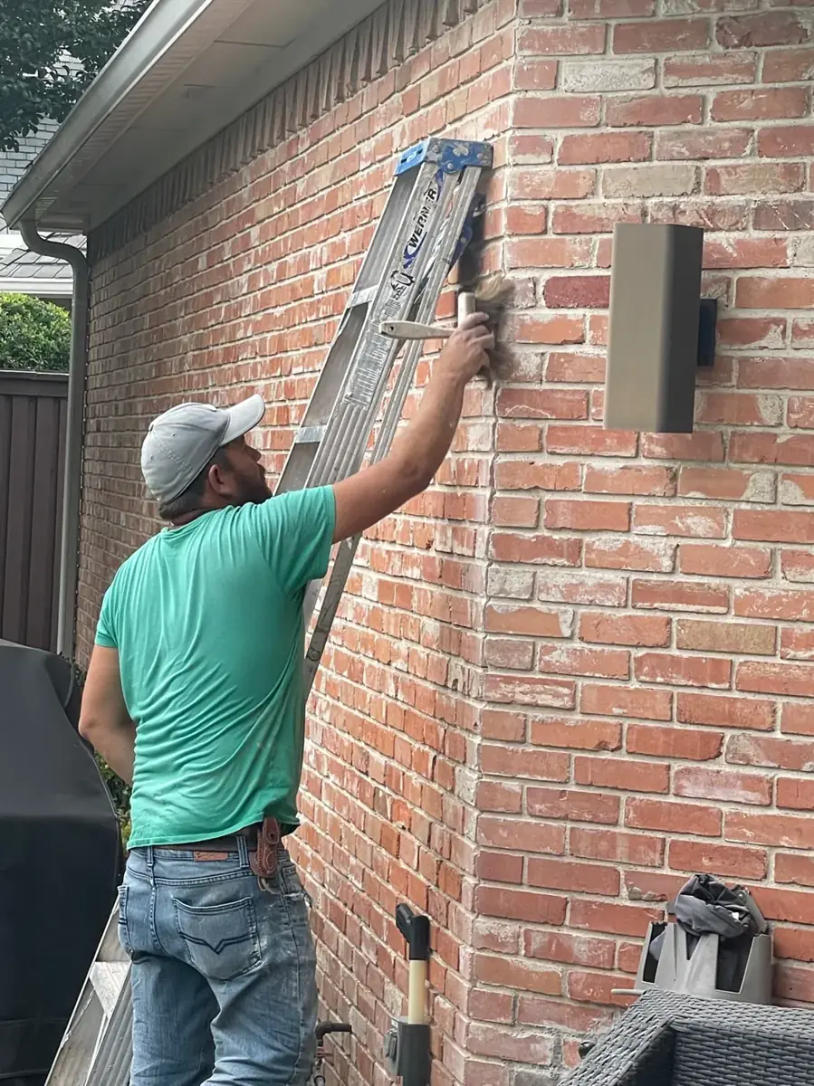 Mason on a ladder tuckpointing a red brick wall